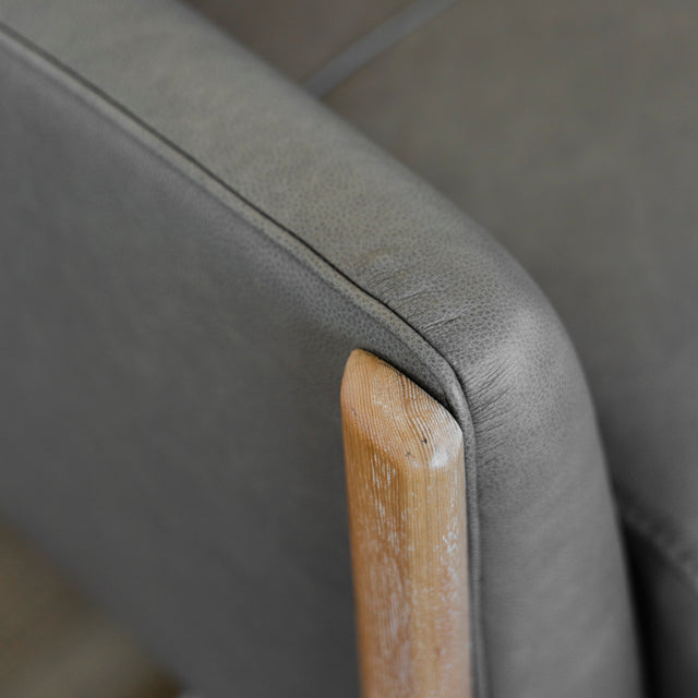 detail de l accoudoir en cuir gris et finition en bois clair du fauteuil.
