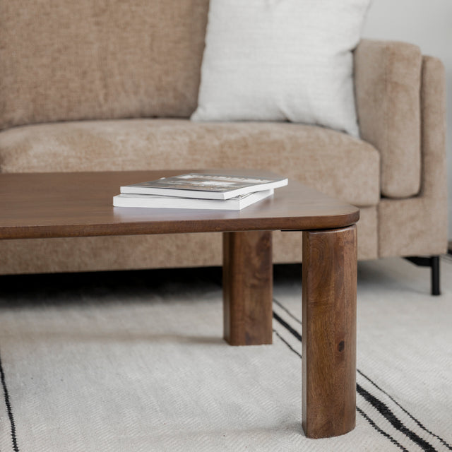 Table basse en bois fonce avec pieds ronds devant canape beige sur tapis clair.