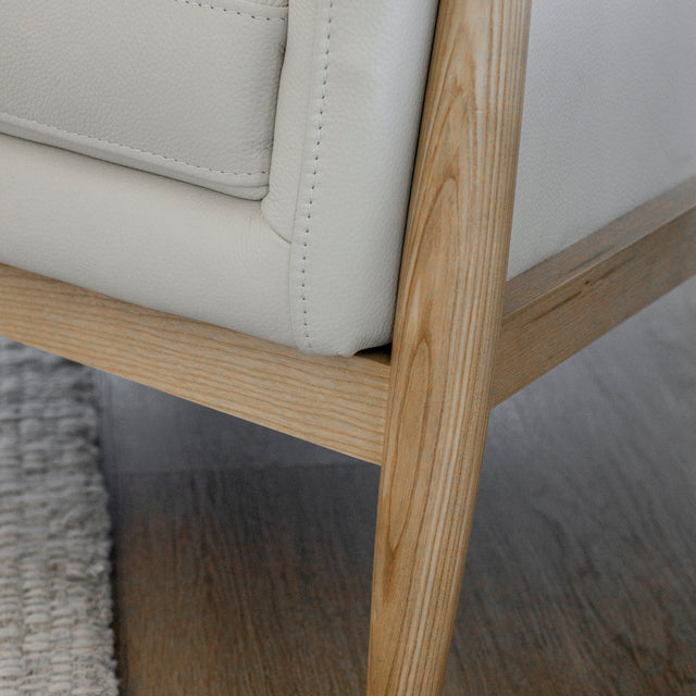 Image rapprochée d'un fauteuil en cuir crème avec structure en bois clair dans un salon lumineux.