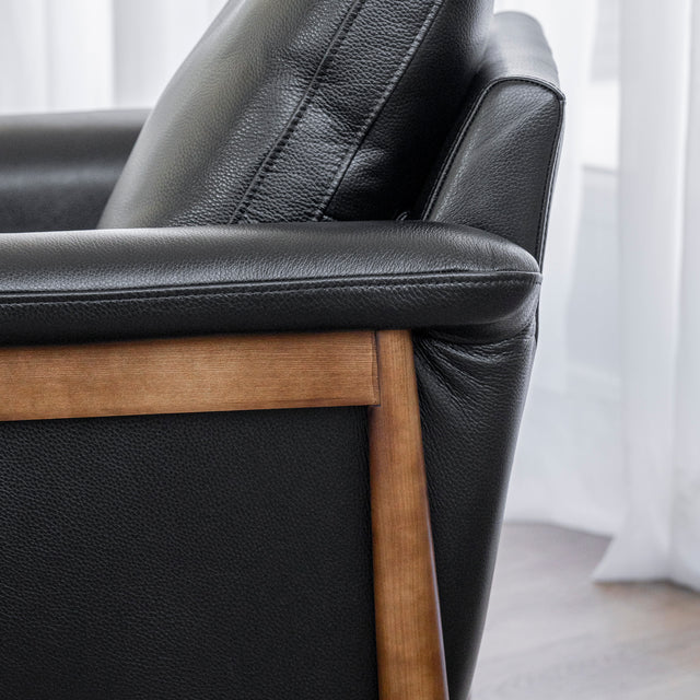 Image rapprochée d'un fauteuil en cuir noir avec structure en bois dans un salon moderne.
