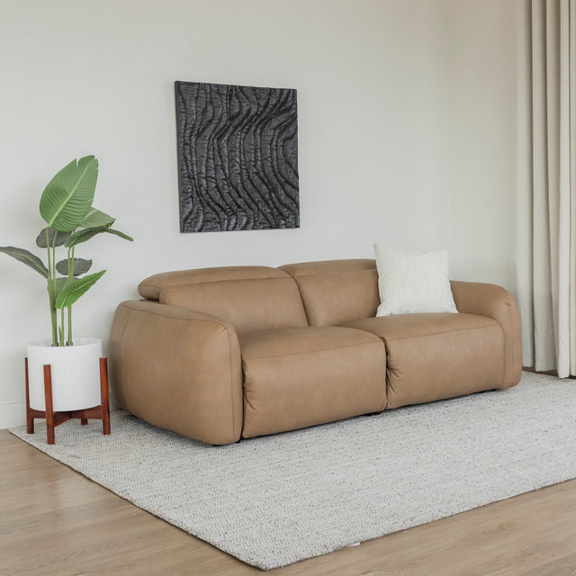 canape en cuir beige clair design moderne avec coussin creme et plante verte sur tapis clair.