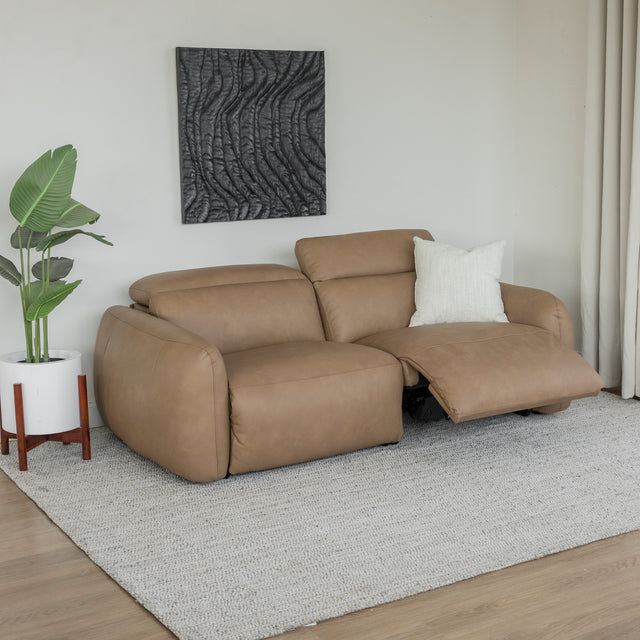 canape inclinable en cuir beige clair avec repose pieds ouvert et coussin creme sur tapis clair.