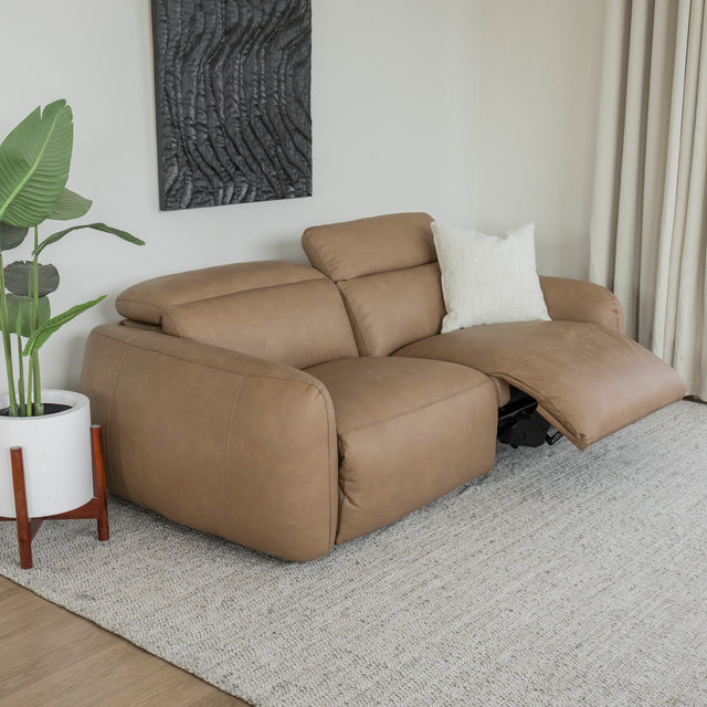 canape inclinable en cuir beige clair avec repose pieds ouvert et coussin creme sur tapis clair.