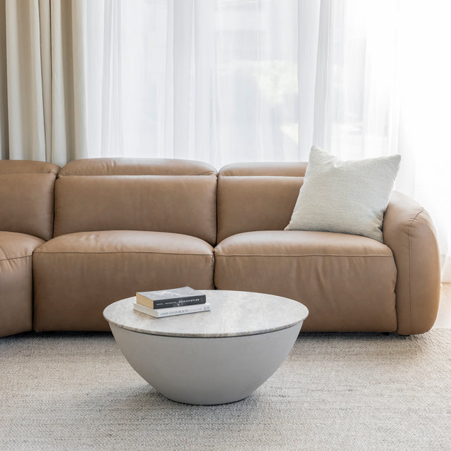 canape en cuir beige clair avec coussin creme et table basse ronde en pierre sur tapis clair.