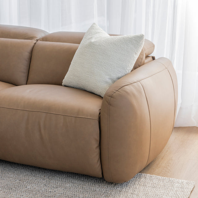 zoom sur l accoudoir arrondi du canape en cuir beige clair avec coussin texture creme et rideaux blancs en arriere plan.