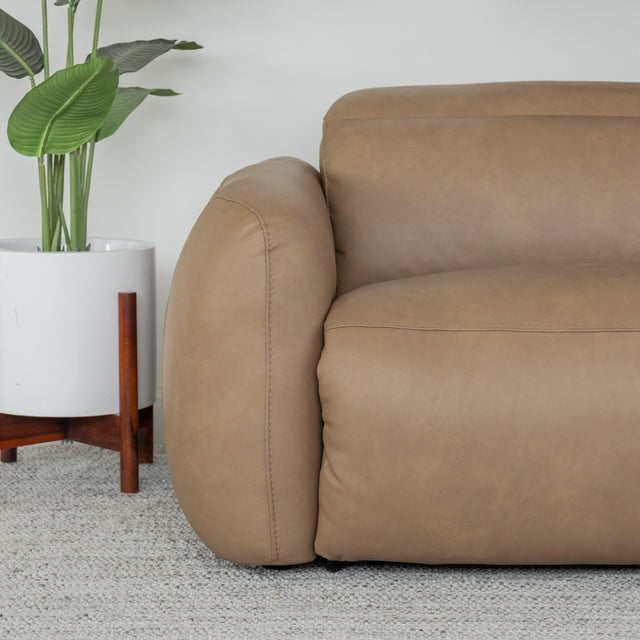 gros plan sur l accoudoir du canape en cuir beige clair avec coutures fines et plante decorative a cote.