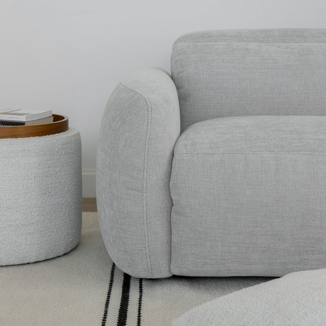 zoom sur l accoudoir du canape gris clair en tissu avec table d appoint ronde a cote.