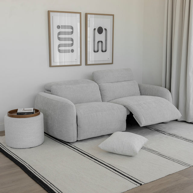 canape gris clair deux places avec dossier inclinable et repose pieds ouvert sur tapis clair.