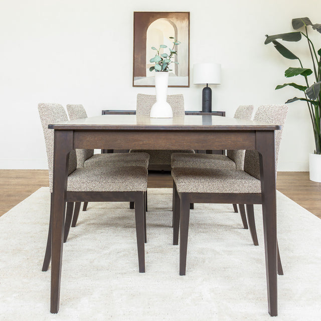 Table à manger rectangulaire en bois foncé avec six chaises rembourrées dans une salle à manger lumineuse.