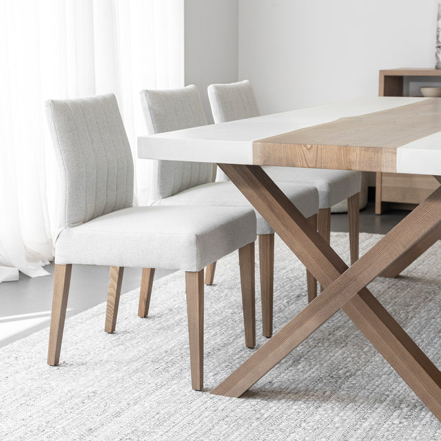 table de salle a manger moderne avec plateau en bois et resine blanche, pieds croises en bois clair et chaises beige sur tapis tissé clair.