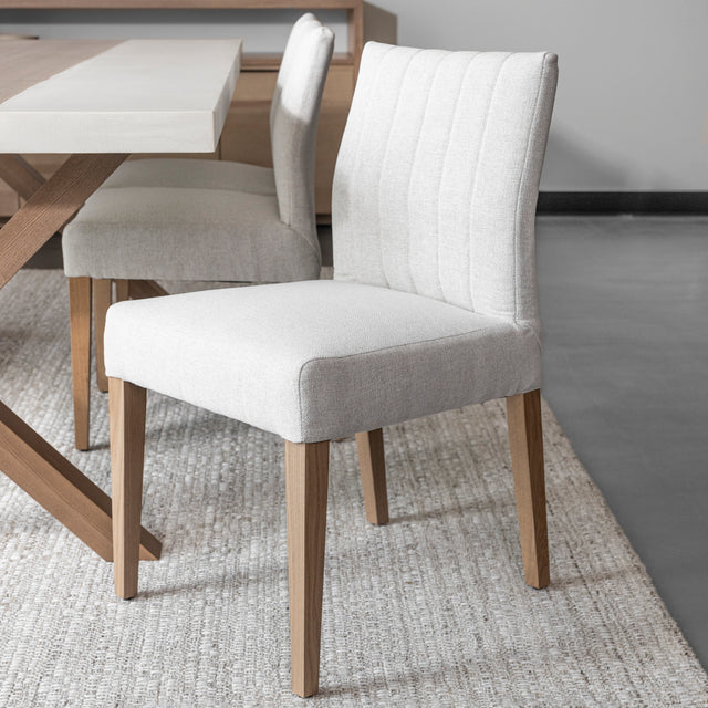 chaise de salle a manger moderne avec assise et dossier rembourrés en tissu beige clair et pieds en bois naturel.