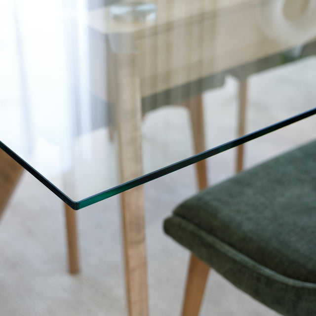 Table à manger en verre avec pieds en bois et chaises en tissu vert, style moderne dans un intérieur lumineux.