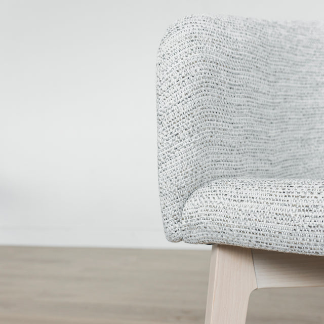 Image rapprochée d'une chaise moderne en tissu crème avec pieds en bois clair dans une salle a manger minimaliste.