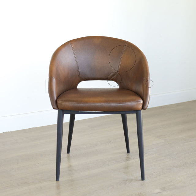Chaise moderne en cuir cognac avec dossier incurvé et pieds noirs élegants avec cercles indiquant les défauts.