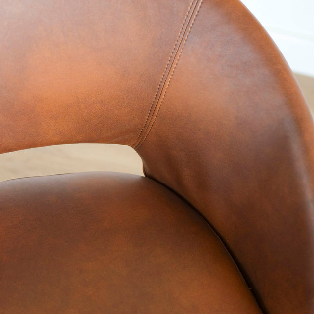 Image rapprochée d'une chaise moderne en cuir cognac avec dossier incurvé et pieds noirs élegants.