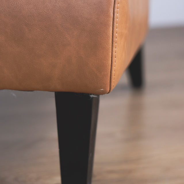 Image rapprochée d'un fauteuil moderne en cuir végane cognac avec pieds noirs sur sol en bois.