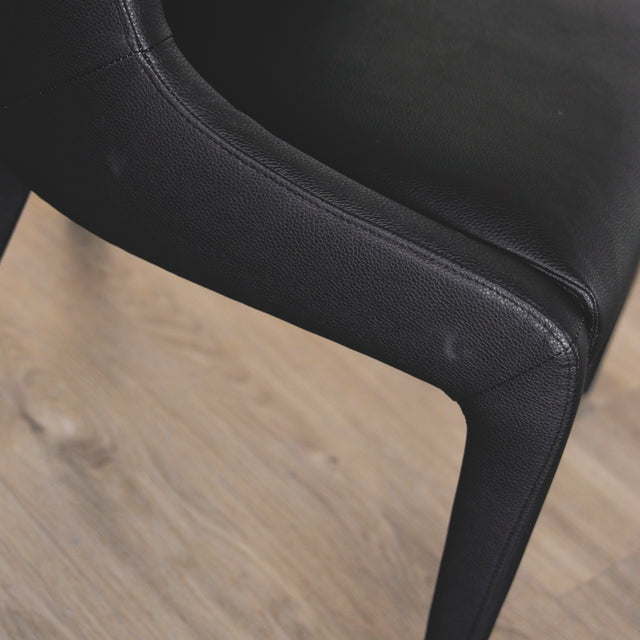 image rapprochée d'une chaise contemporaine en cuir végane noir avec design incurve et pieds assortis.