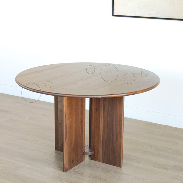 Table ronde en noyer massif avec pied central croise au design contemporain avec cercle indiquant les défauts.