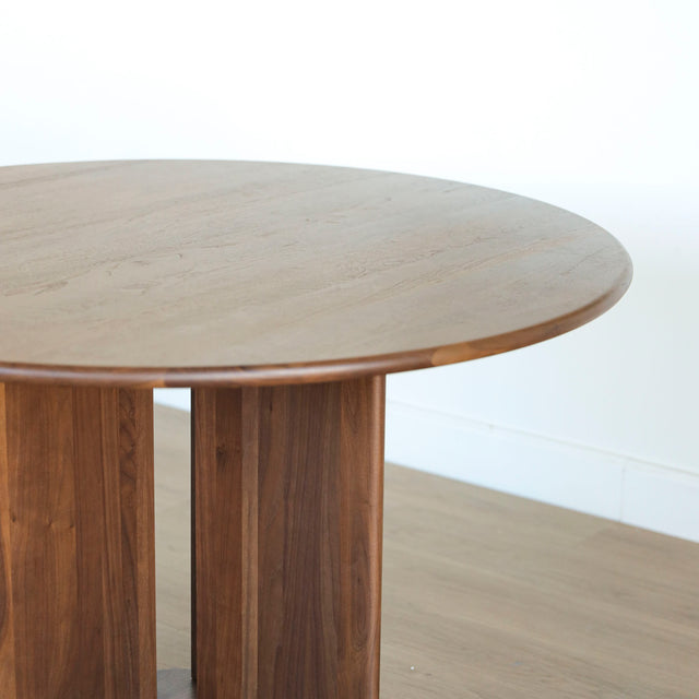 Table ronde en noyer massif avec pied central croise au design contemporain.