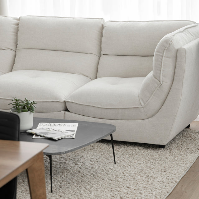 Angle du canape sectionnel blanc moderne avec table basse noire sur tapis texture clair.