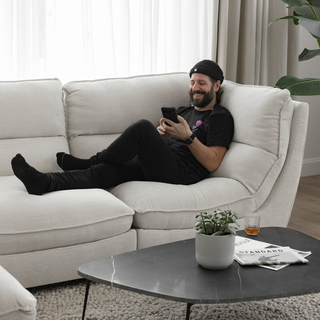 Canape sectionnel blanc moderne avec table basse noire et personne detendue utilisant son telephone.