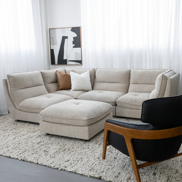 Canape sectionnel beige moderne avec pouf assorti et fauteuil noir sur grand tapis clair.