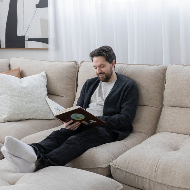 Canape sectionnel beige moderne avec personne detendue lisant un livre dans salon lumineux.