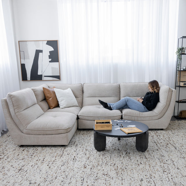 Canape sectionnel beige moderne avec table basse noire et personne detendue sur tapis clair.