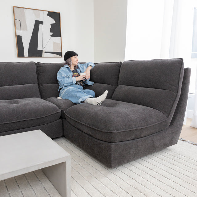 Canape sectionnel gris moderne avec table basse beton et personne detendue tenant une tasse.