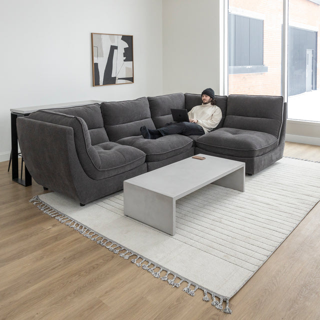 Canape sectionnel gris moderne avec table basse beton et personne travaillant sur ordinateur portable.