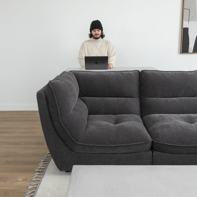 Canape sectionnel gris moderne avec personne travaillant sur ordinateur derriere le sofa.