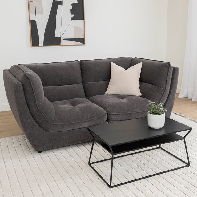 Canape deux places gris moderne avec coussin beige et table basse noire sur tapis clair.