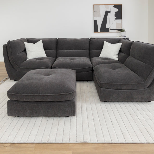Canape sectionnel gris fonce avec pouf assorti sur tapis beige dans salon lumineux.
