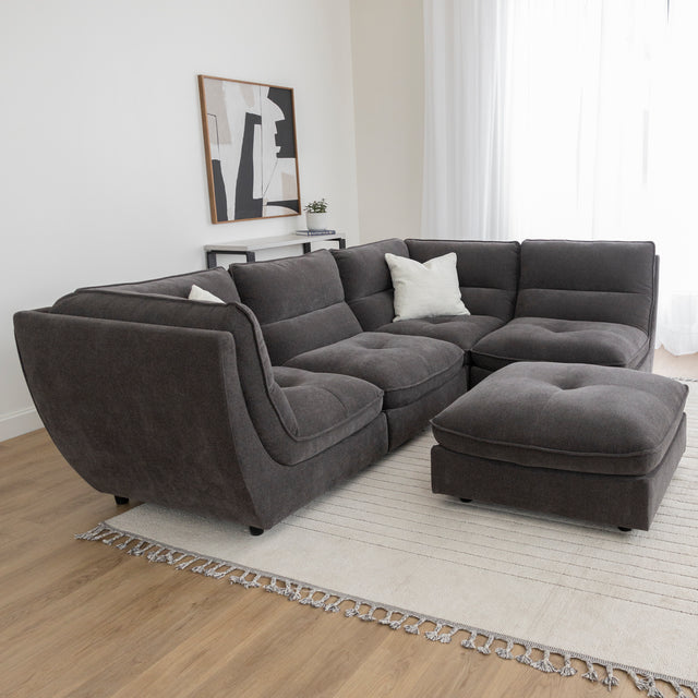 Canape sectionnel gris fonce avec pouf assorti sur tapis beige dans salon lumineux.