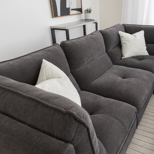 Canape sectionnel gris fonce en tissu avec coussins beiges dans salon moderne.