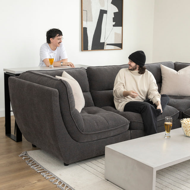 Canape sectionnel gris moderne avec table basse beton et deux personnes discutant detendues.
