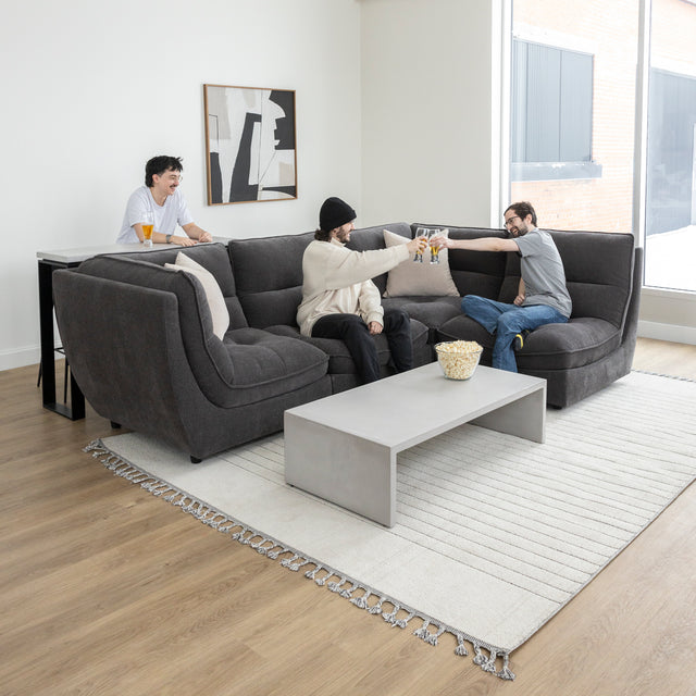 Canape sectionnel gris moderne avec table basse beton et amis partageant un moment convivial.