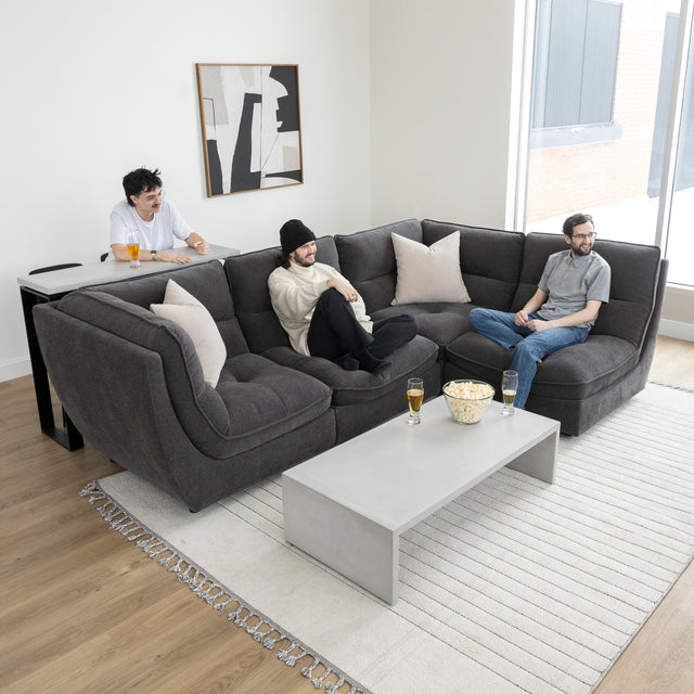 Canape sectionnel gris moderne avec table basse beton et amis partageant un moment convivial.