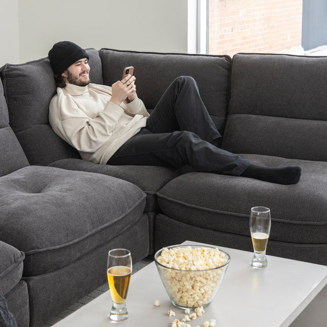 Canape sectionnel gris moderne avec table basse et personne detendue regardant son telephone.