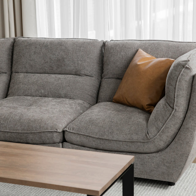 Angle du canape sectionnel gris moderne avec coussin brun et table basse bois.