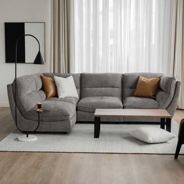 Canape sectionnel gris moderne avec coussins brun et creme, table basse bois et lampe noire.