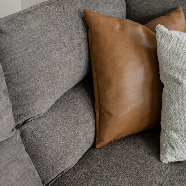 Gros plan sur canape gris moderne avec coussins decoratifs brun cuir et creme texture.