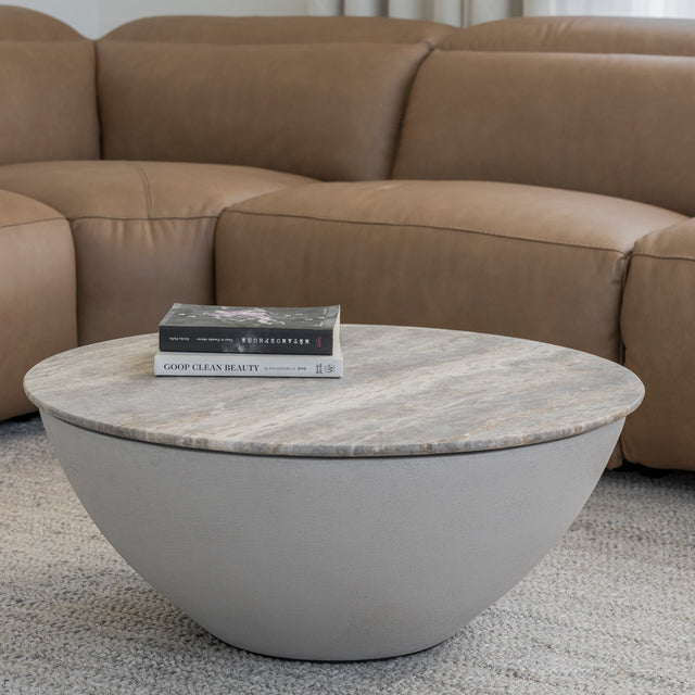 Table basse ronde en beton avec plateau effet pierre devant canape en cuir brun.