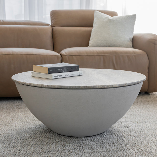 Table basse ronde en beton avec plateau effet pierre devant canape en cuir brun.