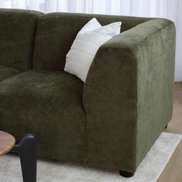 Sectionnel en tissu vert olive avec méridienne gauche, au design arrondi et contemporain dans un salon lumineux.