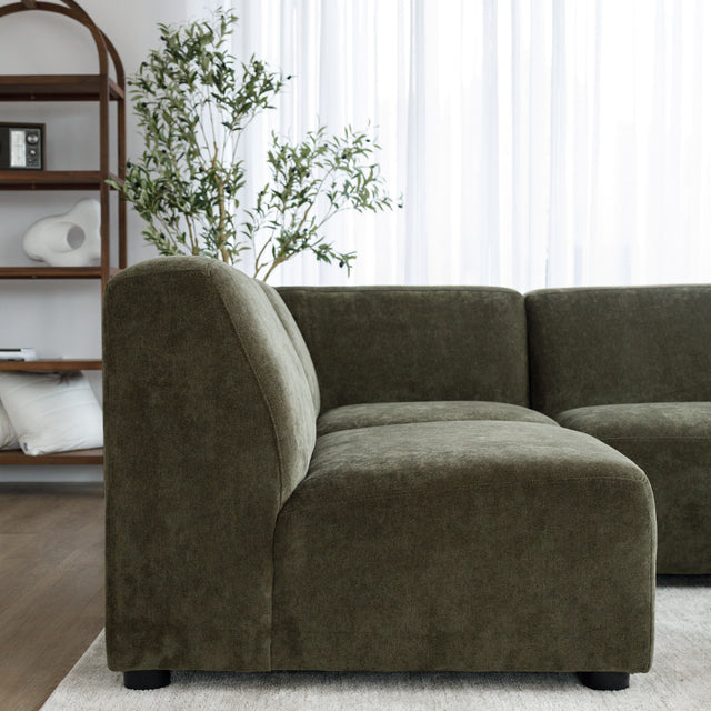 Sectionnel en tissu vert olive avec méridienne gauche, au design arrondi et contemporain dans un salon lumineux.