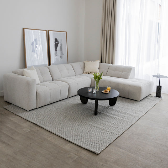 Salon lumineux avec canape d angle beige clair matelasse et table basse ronde noire.