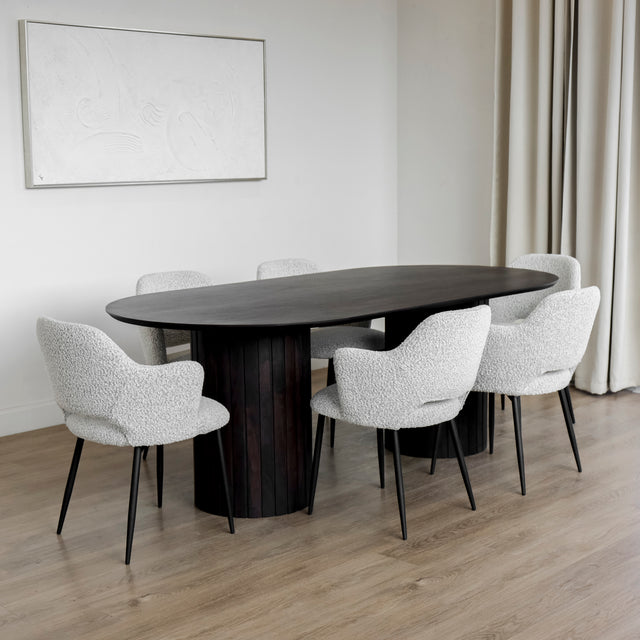 Table a diner ovale en bois fonce avec six chaises en tissu boucle blanc et pieds noirs.