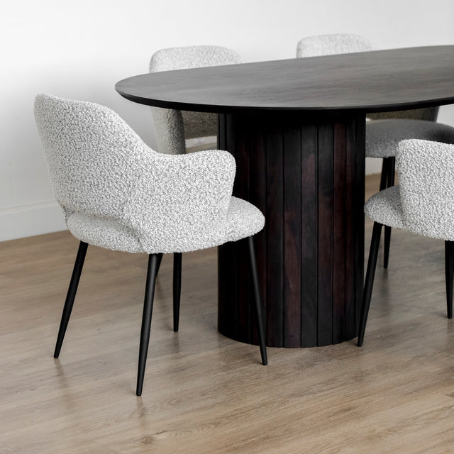 Table a diner ovale en bois fonce avec six chaises en tissu boucle blanc et pieds noirs.
