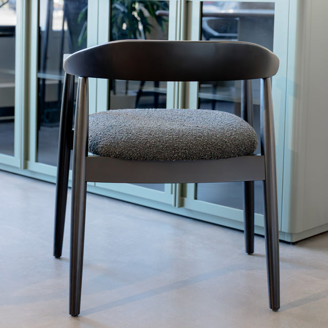 Chaise de salle à manger contemporaine avec accoudoirs noirs et assise rembourrée en tissu texturé gris.